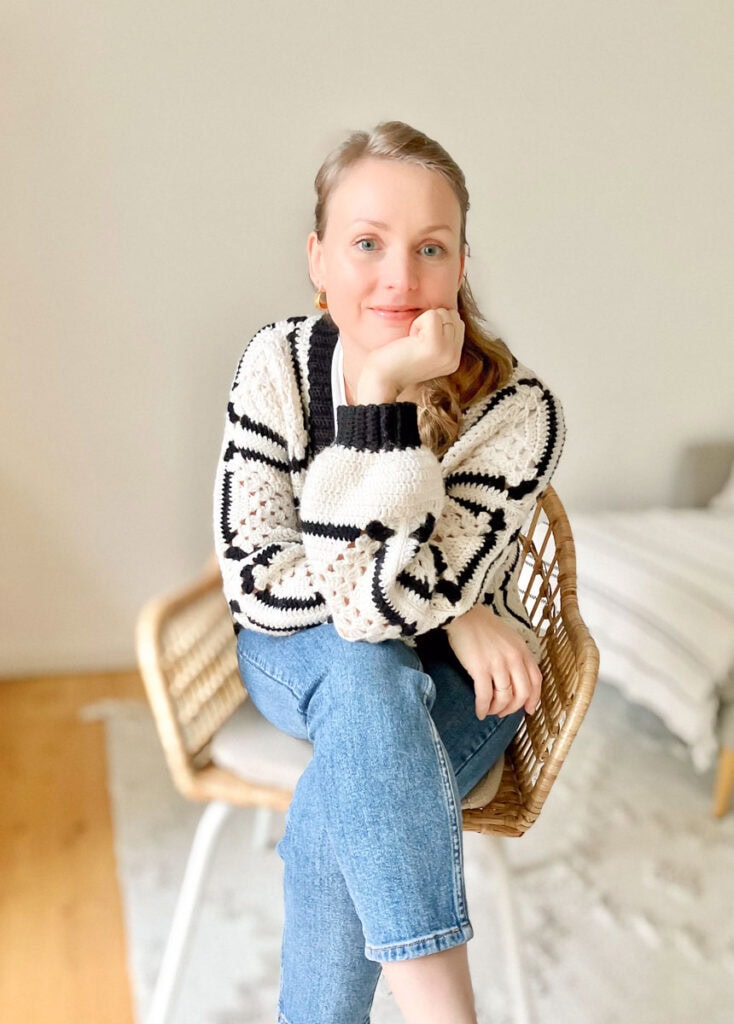 Woman sitting on a wicker chair with a cozy crochet sweater, showcasing modern free crochet patterns.