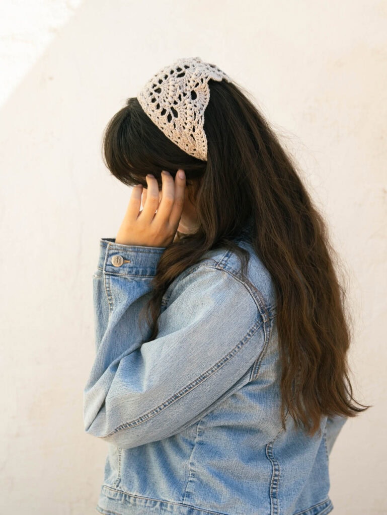 Woman wearing a cream crochet bandana from the side with long dark hair and a denim jacket