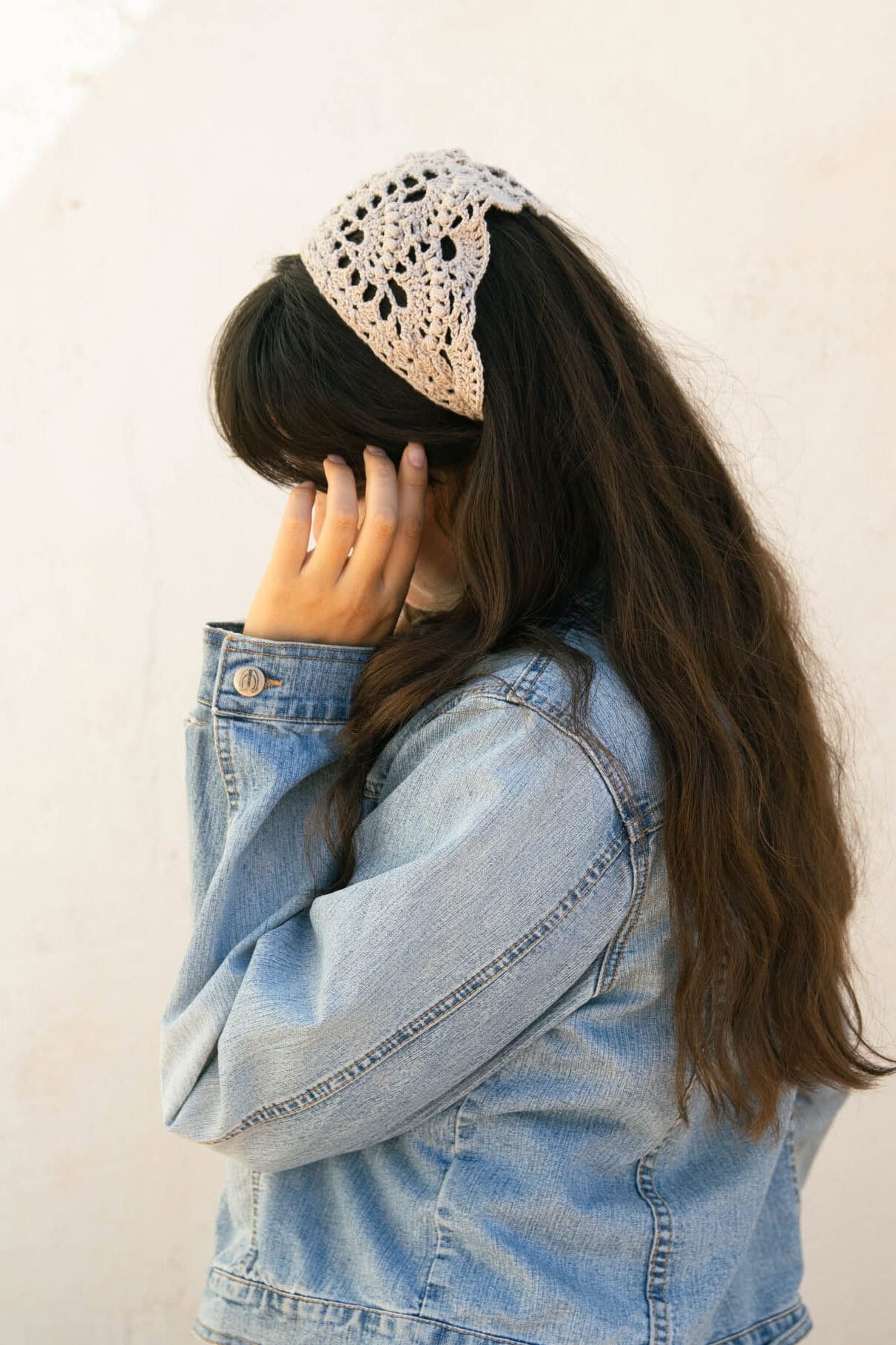 Woman wearing a cream crochet bandana from the side with long dark hair and a denim jacket